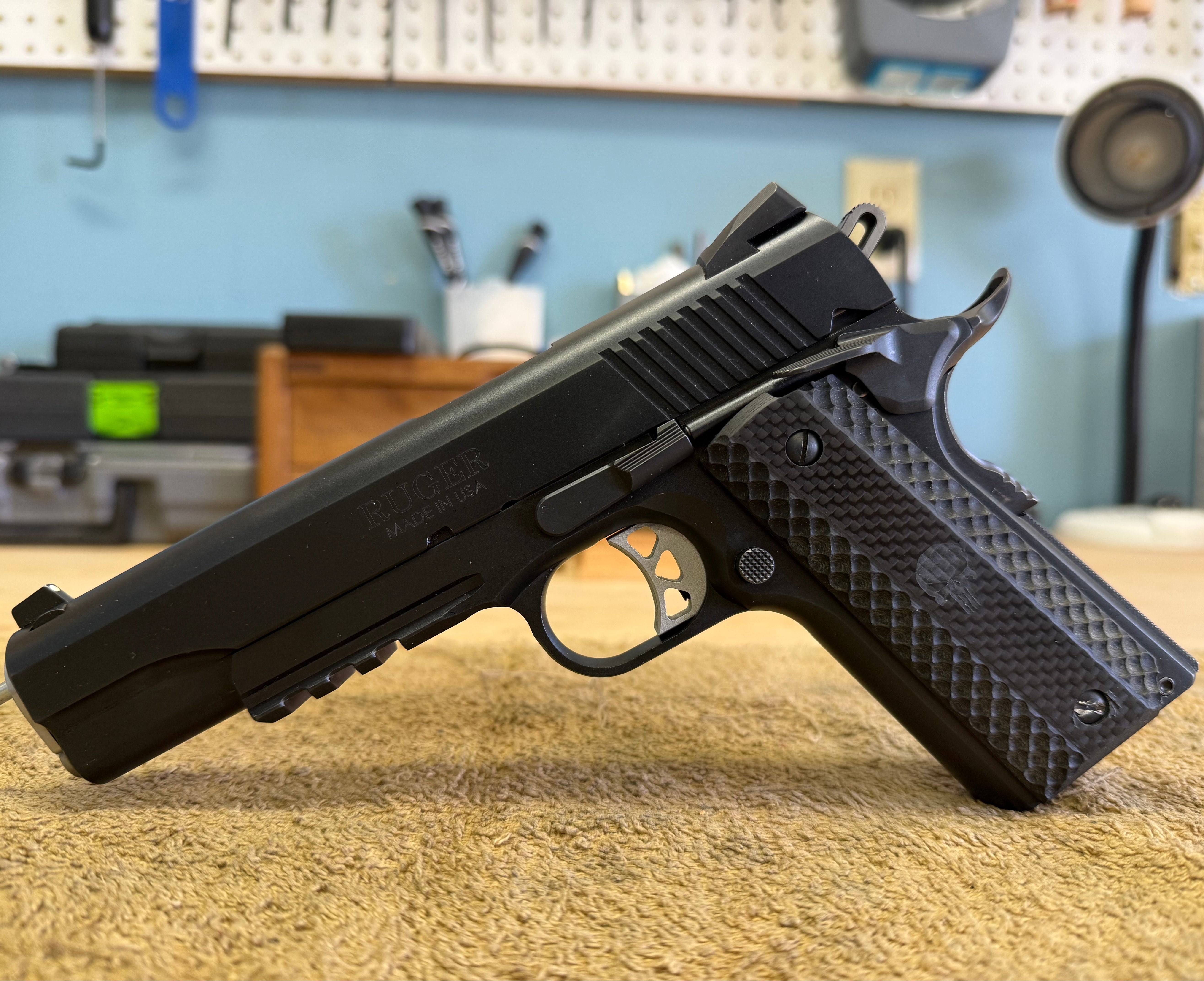 Black 1911 handgun on a textured surface with a workshop background